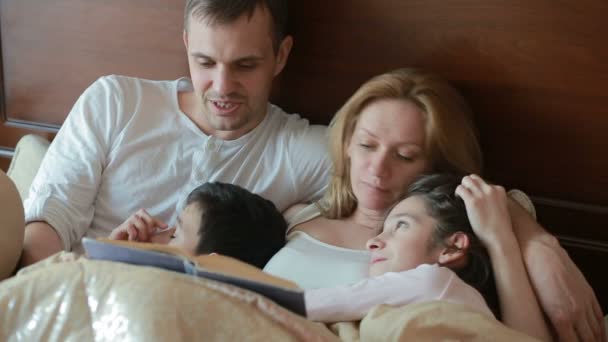 Familia feliz en la cama leyendo un libro en voz alta en casa — Vídeos de Stock