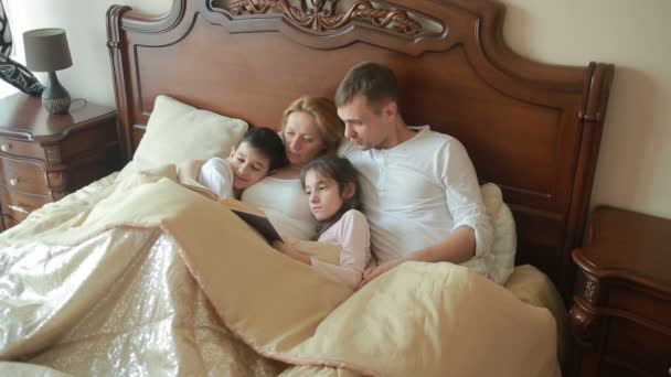 Heureuse famille au lit lisant un livre à haute voix à la maison — Video