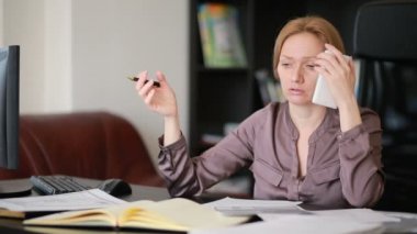 Bir bilgisayar ve Office belgeleri ile çalışan çekici kadın telefonda konuşurken