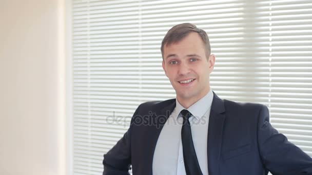 オフィス カーテン カメラ目線と笑顔の背景に立っている若い実業家 — ストック動画