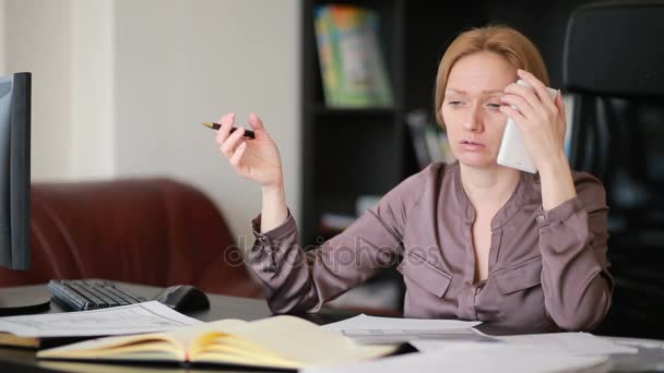 Mulher de negócios atraente trabalhando com um computador e documentos no escritório, falando ao telefone — Vídeo de Stock