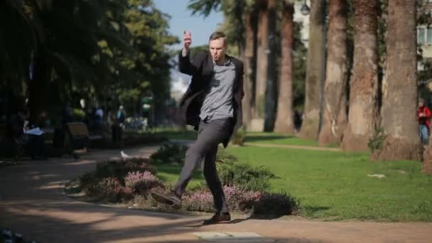Šťastný podnikatel v kabátě a s kufrem tančí šťastně venku na pozadí palem. — Stock video