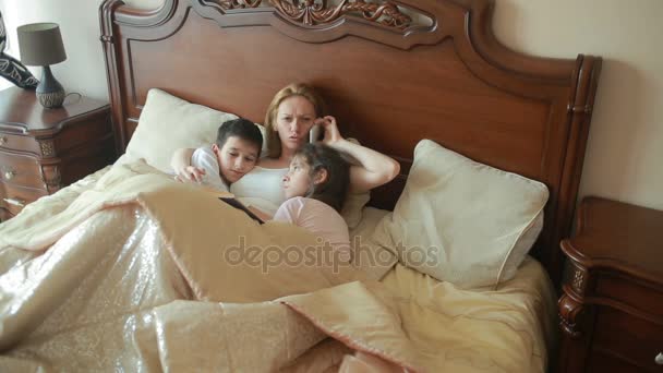 Щаслива сім'я на ліжку читає книгу вголос вдома — стокове відео
