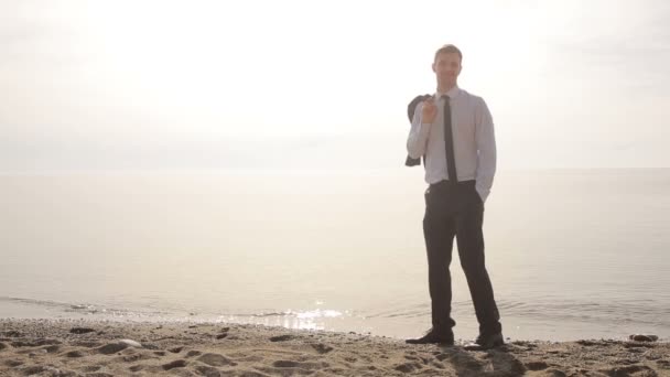 Zakenman wandelingen langs het strand in een pak. bewondert het mooie strand — Stockvideo