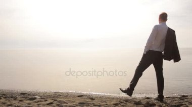 İşadamı elbiseli bir plaj boyunca elini kolunu sallaya dönüyor. güzel plaj hayran