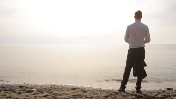 Zakenman wandelingen langs het strand in een pak. bewondert het mooie strand — Stockvideo