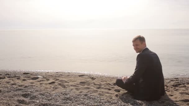 Zakenman in pak zittend op het strand het gooien van stenen in het water en gebaren nodigt aan zichzelf — Stockvideo