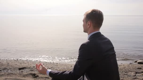 Zakenman in pak zit op het zand en mediteert op het strand — Stockvideo