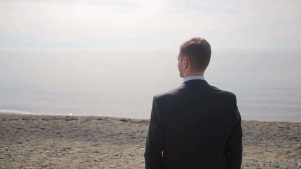Uomo d'affari passeggia lungo la spiaggia con un completo. ammira la bellissima spiaggia — Video Stock