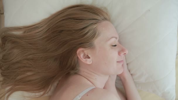 La mujer está acostada en la cama y sonriendo mientras duerme. Primer plano. vista desde arriba — Vídeos de Stock