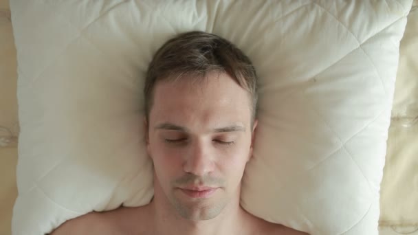 En man ligger på sängen och kraftigt öppnar ögonen, ser in i kameran. Närbild. Visa från ovan — Stockvideo