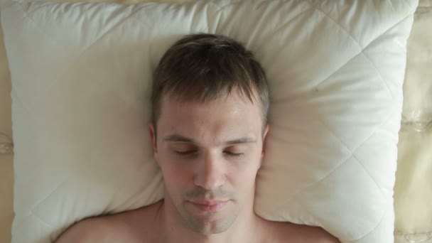 Muž leží na posteli a prudce otevře oči, podívá do kamery a úsměvy. Detail. Pohled shora — Stock video