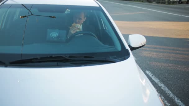 Empresario comiendo comida rápida sentado al volante de un coche — Vídeo de stock