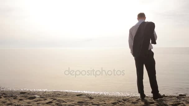 Бізнесмен у костюмі стоїть на пляжі і жестикулює, запрошуючи приєднатися до себе — стокове відео