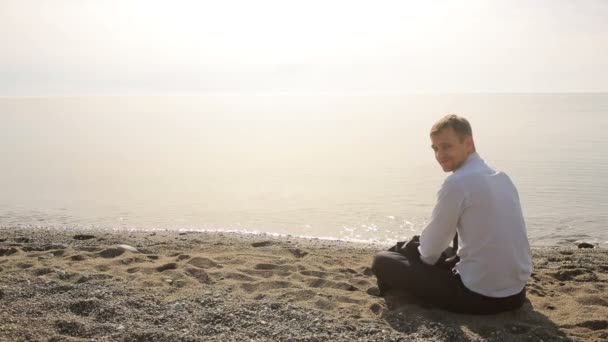 Uomo d'affari in giacca e cravatta seduto sulla spiaggia e gesticolare invitando a unirsi a se stesso — Video Stock