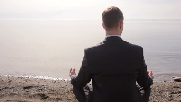 Бізнесмен у костюмі сидить на піску і медитує на пляжі — стокове відео