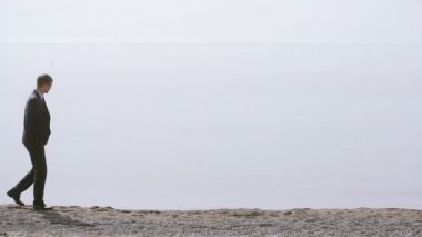 İşadamı elbiseli bir plaj boyunca elini kolunu sallaya dönüyor. güzel plaj hayran