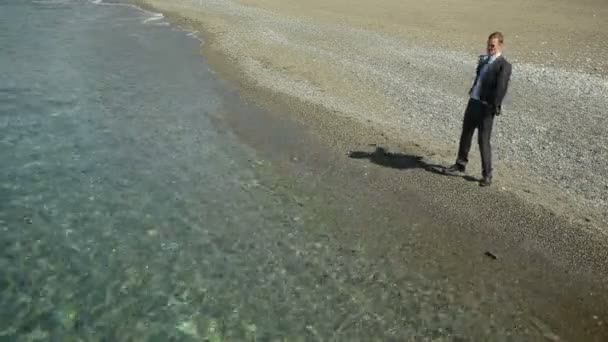 Hombre de negocios en traje de pie en la playa y el gesto, invitando a seguir adelante. Extiende su mano hacia adelante — Vídeos de Stock