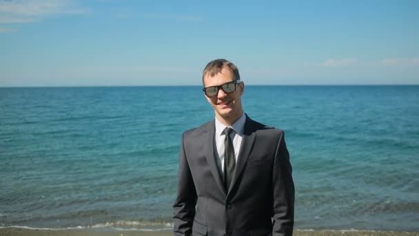 Επιχειρηματίας περπάτημα στην παραλία σε ένα κοστούμι. Εξετάζει τα φωτογραφικών μηχανών και χαμόγελα — Αρχείο Βίντεο