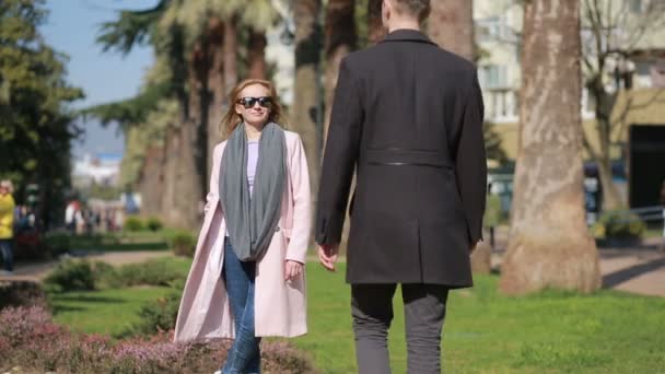 Un couple heureux amoureux qui s'amuse. Jolie belle femme avec un bel homme dans un manteau embrassant. Sur fond de palmiers et d'arbres . — Video
