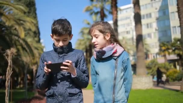 Les enfants marchent le long de l'avenue dans le parc et sont occupés avec leurs téléphones — Video