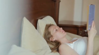 Güzel genç kadın yatakta üzücü bir kitap okuma