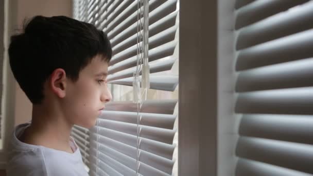 Мальчик смотрит на улицу из окна через жалюзи — стоковое видео