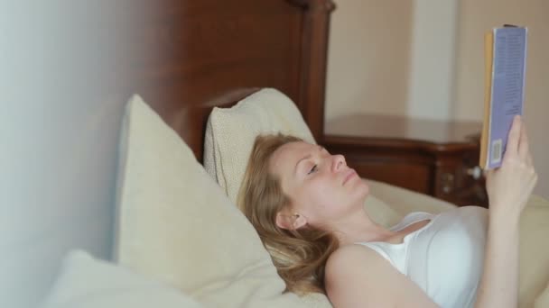 Hermosa joven leyendo un libro triste en la cama — Vídeos de Stock