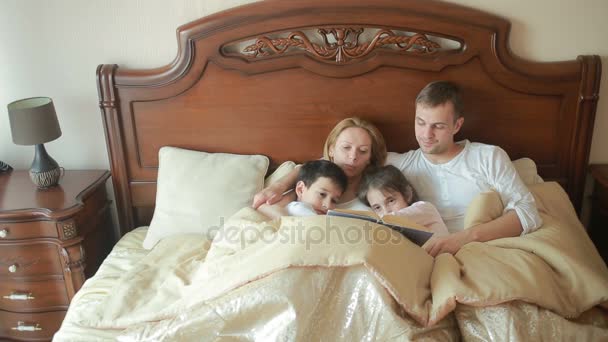 Ευτυχισμένη οικογένεια σε κρεβάτι διαβάζοντας ένα βιβλίο δυνατά στο σπίτι — Αρχείο Βίντεο