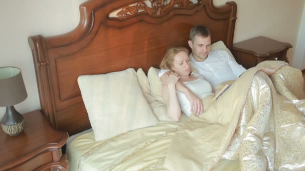 Mann und Frau liegen auf dem Bett im Schlafzimmer und lesen gemeinsam das Buch vor — Stockvideo