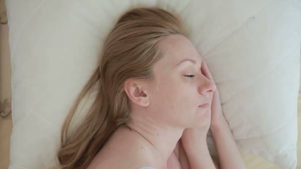 Женщина лежит на кровати и улыбается во сне. крупным планом. вид сверху — стоковое видео