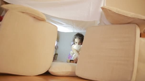 Una bambina è seduta in una casa improvvisata di cuscini e una casa coperta — Video Stock