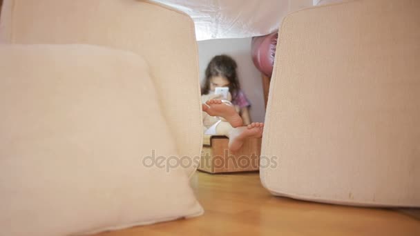 Una niña está sentada en una casa improvisada de almohadas y una casa de mantas — Vídeos de Stock