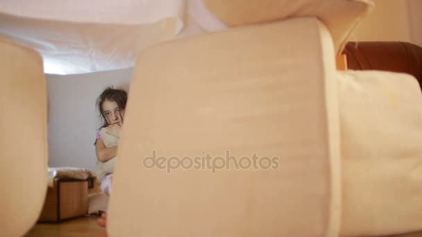 Una niña está sentada en una casa improvisada de almohadas y una casa de mantas — Vídeos de Stock