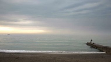 Bir iskelede günbatımında deniz, zaman atlamalı kıyısında insan siluetleri