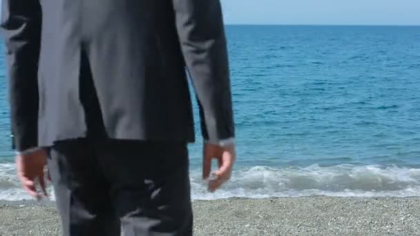 Uomo d'affari passeggia lungo la spiaggia con un completo. ammira la bellissima spiaggia — Video Stock