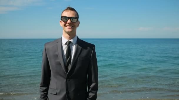 Homme d'affaires marchant sur la plage en costume. Admet la belle plage. Il regarde la caméra et rit, il est heureux — Video