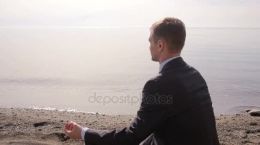 İş takım elbiseli adamı kum üzerine oturur ve sahilde meditasyon