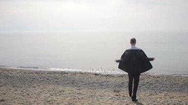 İşadamı plajda, ceketini, kapalı alır ayakta takım elbiseyle kravat ve gömlek unbuttons