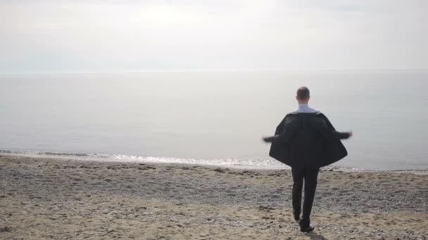 Businessman in suit standing on beach, takes off his jacket, tie and unbuttons shirt — Stock Video