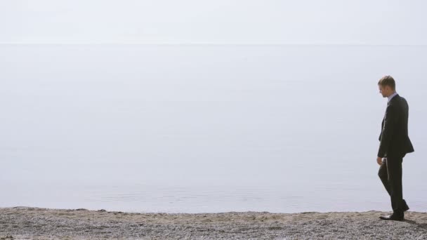 Zakenman wandelingen langs het strand in een pak. bewondert het mooie strand — Stockvideo