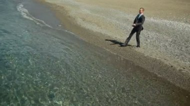 İşadamı elbiseli bir plaj boyunca elini kolunu sallaya dönüyor. güzel plaj hayran