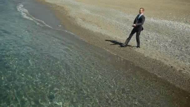 Бизнесмен прогуливается по пляжу в костюме. восхищается красивым пляжем — стоковое видео