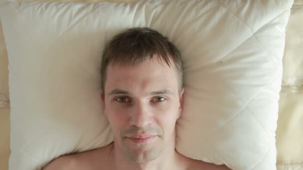 Мужчина лежит на кровати и резко открывает глаза, смотрит в камеру и улыбается. Крупный план. Вид сверху — стоковое видео