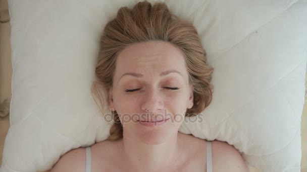 Una mujer acostada en una cama abre los ojos y sonríe. Primer plano. Vista desde arriba — Vídeo de stock