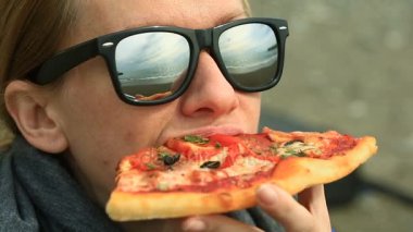 Bir kadın yalnız kötü havada ıssız bir kumsalda oturur, denize görünüyor ve pizza yiyor