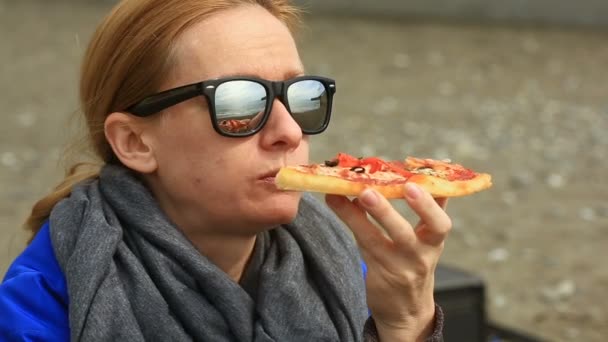 Eine Frau sitzt bei schlechtem Wetter allein an einem einsamen Strand, blickt aufs Meer und isst Pizza — Stockvideo