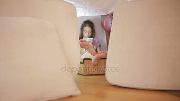 小さな女の子は枕の仮設ハウスと毛布の家に座っています。 — ストック動画