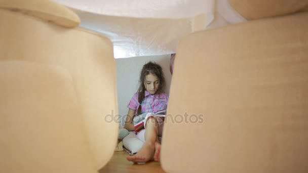 Een meisje zit in een geïmproviseerde huis kussens en een deken-huis — Stockvideo