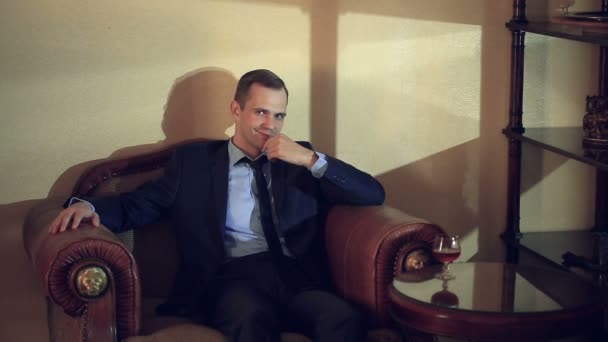 Κτηνώδης άνθρωπος σε ένα κοστούμι που κάθεται σε μια δερμάτινη πολυθρόνα, κοιτώντας την κάμερα και gesticulating. Τα χέρια στο πρόσωπο αγγίζει ένα πηγούνι και ένα μέτωπο, χειρονομίες της σκέψης, λήψης αποφάσεων — Αρχείο Βίντεο